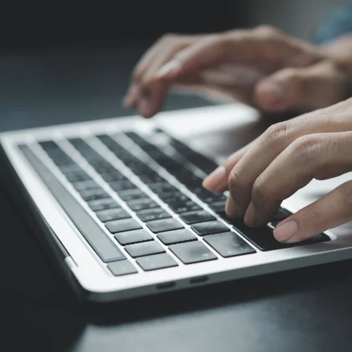 Close-up of hands typing on a laptop keyboard.