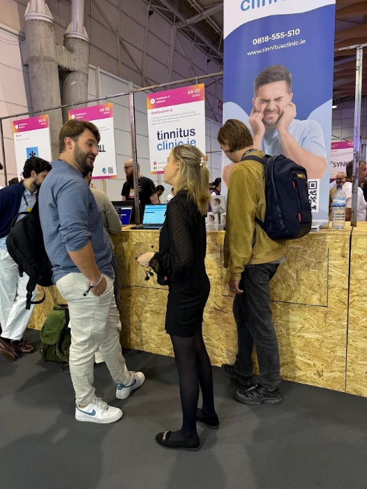 People at a Tinnitus Clinic event booth, with a poster showing a man holding his ears.