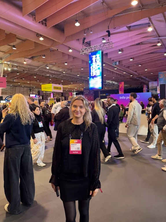 Woman at a tech conference with Alivia badge in a crowded exhibition hall.